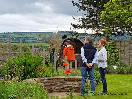 A view of a beautiful garden with a semi-circular stone seat. The client, star and film crew of ‘Love Your Garden’ are enjoying the garden